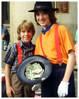 Jay and Sam in their street performer outfits posing with a hat full of money.