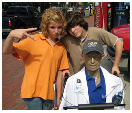 Liza and Isaac push a mannequin in a wheelchair.