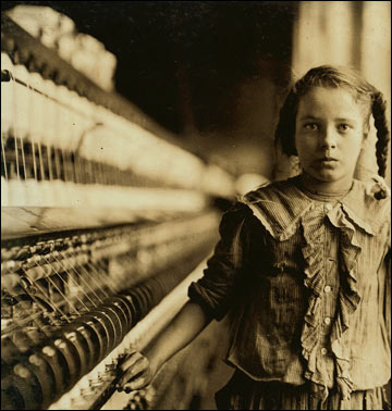 A mill girl next to a huge spinning machine.