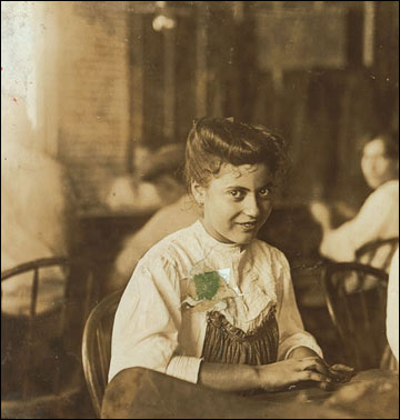 A girl sitting with other kids, rolling cigars.
