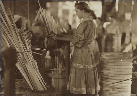 A girl standing in a factory, hammering a basket.