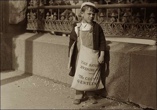 A small boy with a huge bag of newspapers.